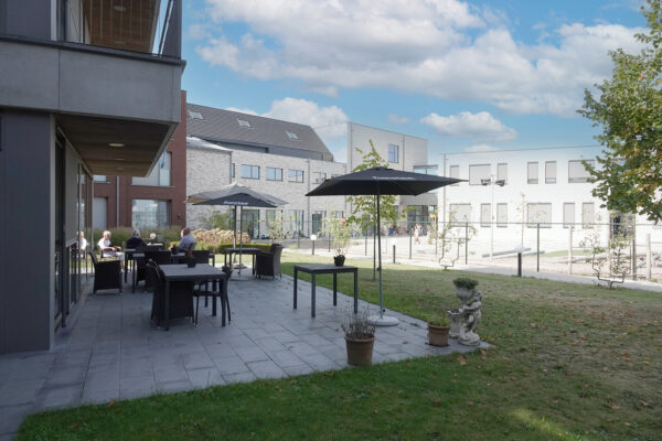 De tuin met terras in woonzorgcentrum Annadal, waar drie bewoners samen zitten op het betegelde terras, uitgerust met zwarte stoelen en tafels.
