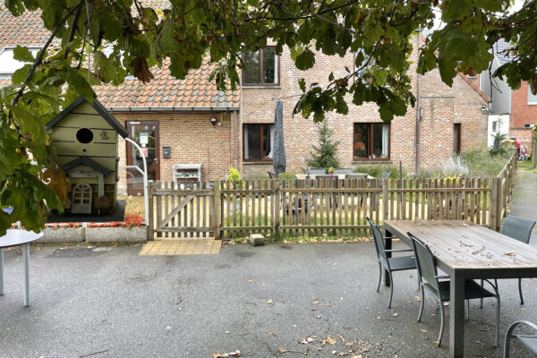 Een buitenpleintje van woonzorgcentrum Anemoon, met tafels en stoelen waar bewoners samen kunnen zitten. Het bakstenen gebouw is zichtbaar op de achtergrond, en het pleintje is direct bereikbaar via een deur.