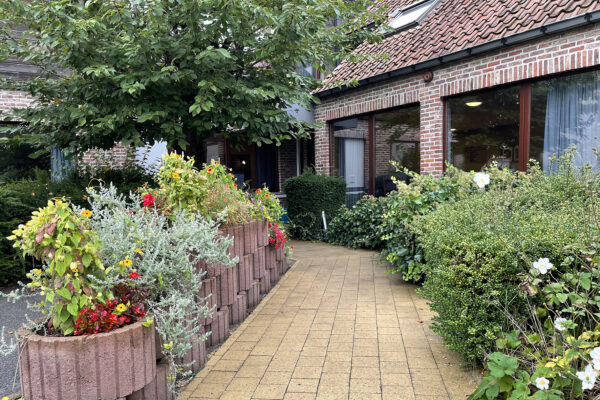Een pad omringd door bloemen in de tuin van woonzorgcentrum Anemoon, met het gebouw zichtbaar naast het pad.