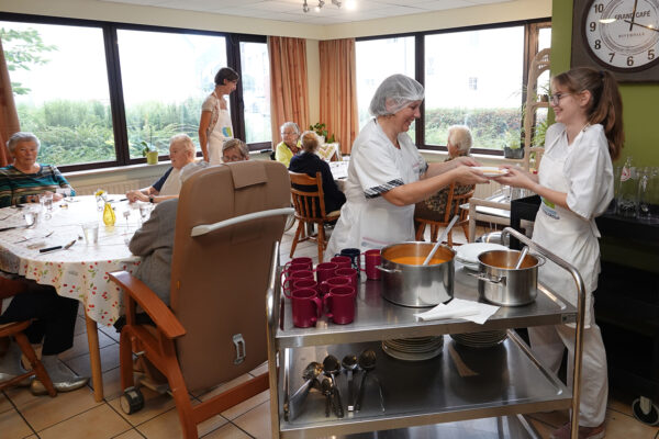 Maaltijdservice in woonzorgcentrum Anemoon, waarbij medewerkers samenwerken om een heerlijke maaltijd te serveren aan bewoners die rond verschillende tafels zitten.