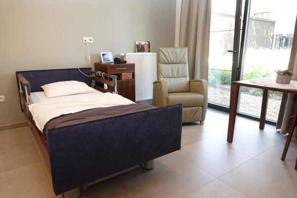 Een slaapkamer in woonzorgcentrum Anemoon, ingericht met een comfortabel bed, een nachtkastje, een tafel en een fauteuil.