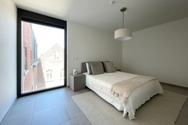 De slaapkamer van een assistentiewoning in Angelahof, modern ingericht met een groot tweepersoonsbed en twee nachtkastjes. De kamer heeft een groot raam waardoor veel natuurlijk licht naar binnen stroomt.