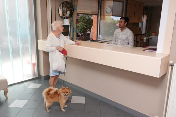 Het onthaal van neuropsychologisch woonzorgcentrum Arcus, waar een bewoner met haar hond de medewerker een vraag stelt.