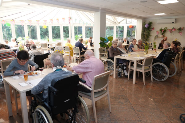 Uitzicht vanuit binnen in woonzorgcentrum De Vlaamse Ardennen naar de veranda, waar bewoners samen kunnen zitten en/of eten, terwijl ze genieten van het buitenzicht en het zonlicht dat naar binnen straalt.