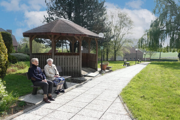 De prieel in de tuin van het woonzorgcentrum De Vlaamse Ardennen. Die zit in de tuin naast een padje. Twee bewoners zitten samen op een bankje.