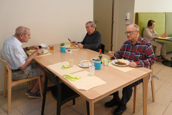 Het restaurant van de assistentiewoningen Ter Bleuk in Rijmenam. Drie bewoners zitten samen aan tafel en genieten van hun maaltijd, die zojuist geserveerd is.