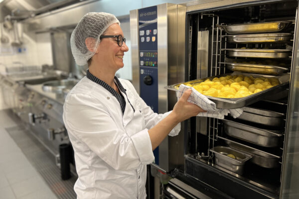 De keuken van woonzorgcentrum Berckenbosch. De kok die een haarnet draagt haalt aardappelen uit een grote stoommachine waarin het eten is verwarmd.