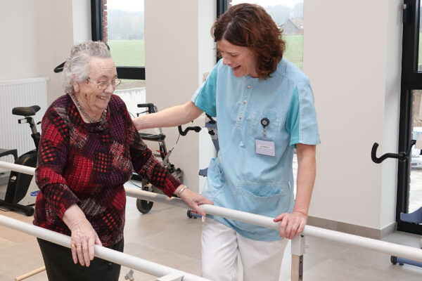Een verpleegster van woonzorgcentrum Berkenhof in Heershelp een vrouwelijke bewoner in haar revalidatie die wandeloefeningen inhoudt. Ze doen de oefeningen in de kinesitherapieruimte van het woonzorgcentrum.
