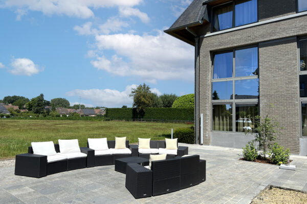 Foto genomen vanuit het terras van het woonzorgcentrum Bruggenpark die kijkt naar de grote tuinbanken van het terras en de grote tuin daarachter. Een klein gedeelte van het gebouw is ook zichtbaar.