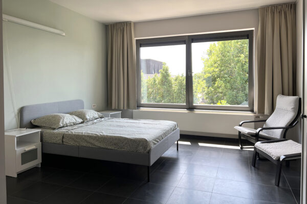 De slaapkamer van een flat in de assistentiewoningen van woonzorgcampus Bruggenpark. De kamer is ingericht met een ligstoel met bijbehorende voetbank, een groot tweepersoonsbed en twee nachtkastjes.