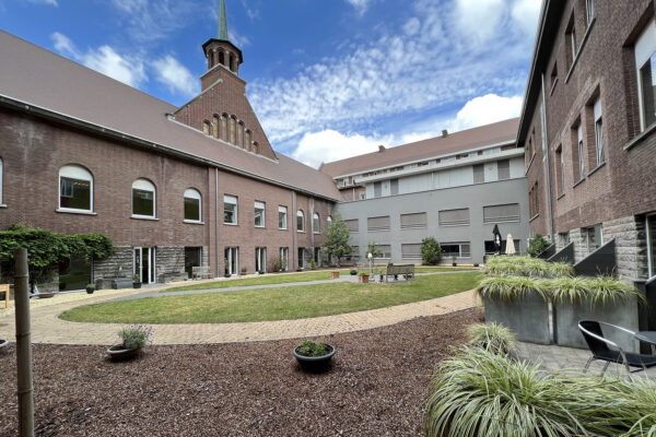 Het binnenplein van woonzorgcentrum Damiaan, bereikbaar vanuit elke kamer op de begane grond. In het midden van het plein staan twee houten banken, met uitzicht op de toren van het bakstenen gebouw.