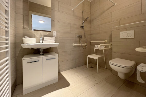 Een modern ingerichte badkamer in een van de assistentiewoningen van Ter Bleuk. De badkamer is voorzien van een lavabo, een toilet met steunbalken en een inloopdouche. Alle oppervlakken zijn bedekt met dezelfde type tegels, wat zorgt voor een uniforme uitstraling.