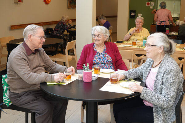 Drie bewoners van de assistentiewoningen Ter Bleuk zitten samen in het restaurant op het terrein, waar ze een hapje eten en iets drinken.