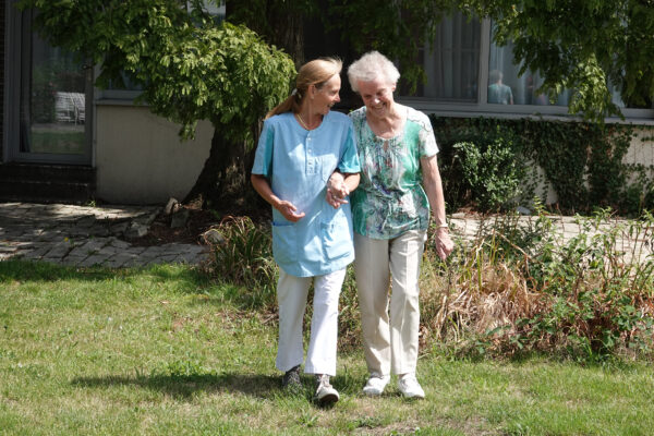 Verzorgende en bewoner wandelen in de tuin