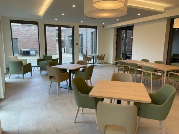 Foto van het Grand Café, genomen vanuit een hoek. Er zijn veel zitplaatsen beschikbaar, met tafels waar mensen alleen, met z'n tweeën, vieren of zessen kunnen zitten.