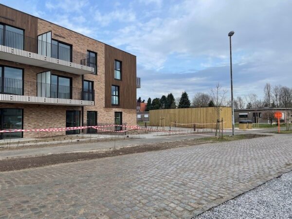 Straatzicht van het woonzorgcentrum Ravestein, waarbij de terrassen van enkele kamers zichtbaar zijn. De gevel is opgebouwd uit baksteen, met houten accenten.