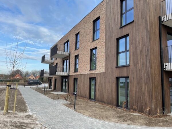 Het woonzorgcentrum Ravestein, gezien vanaf de buitenkant. De gevel heeft houten accenten en de terrassen en een pad zijn duidelijk zichtbaar.