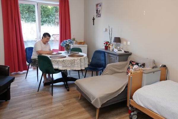Le Progrès - Chambre avec une femme âgée qui écrit, assise à table -Maison de repos - La Louvière