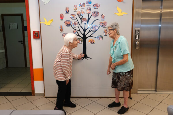 La Passerinette 2 femmes devant un mur de photos et un ascenseur - Maison de repos - Soumagne